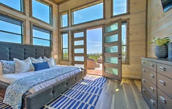 Interior shot of a beautiful and clean room with a blue rug, wooden walls and an open door showcasing a patio with chairs.