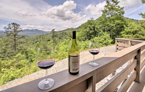 Bottle of wine with glasses on a patio ledge overlooking a beautiful mountain forest