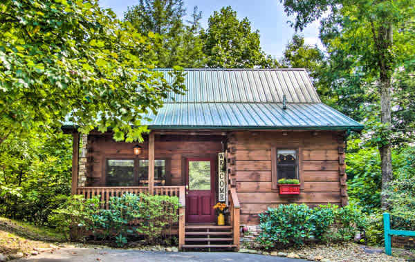 Cute cabin in the woods with a welcome sign and flowers on the porch.