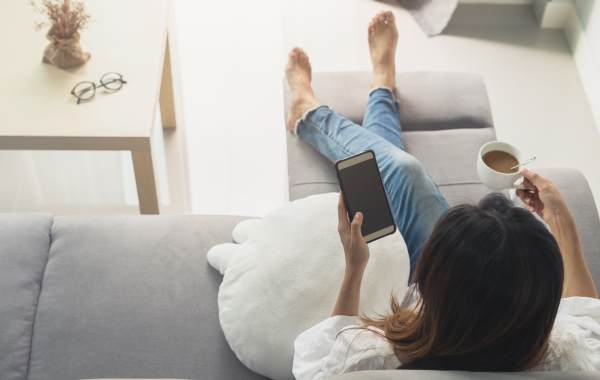 woman sitting on a couch sipping coffee and texting someone