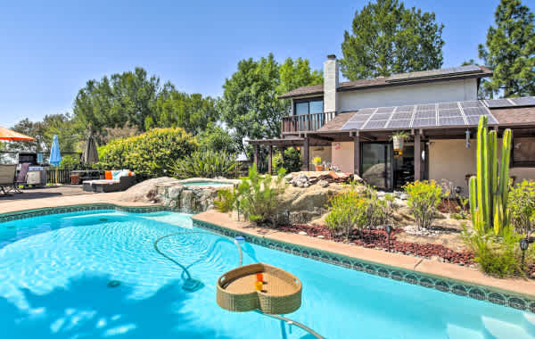 Backyard with a large pool, beautiful foliage, a grill and patio furniture.