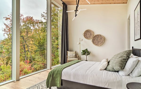 Modern guest bedroom with floor to ceiling windows showcasing an amazing view of a wooded forest.
