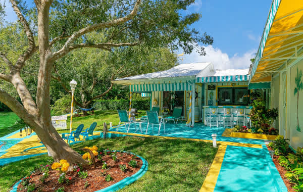 Photo of brightly-colored, mermaid-themed vacation rental backyard with an outdoor bar, set of chairs around a table, and a large leaning tree in Weeki Wachee, FL