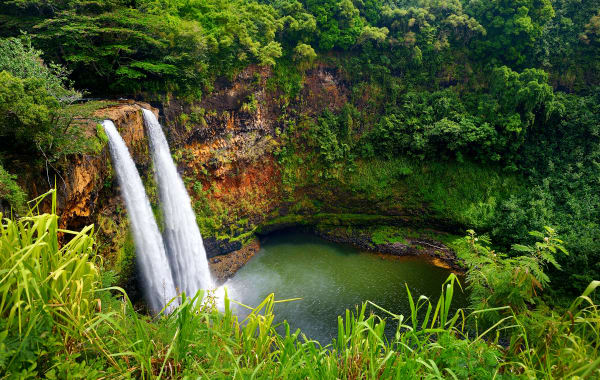 Waterfall and natural pool surrounded by lush green vegetation in Kauai, HI, a great place to own a Hawaii investment property