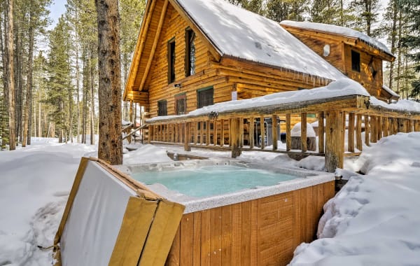 Image of a vacation rental cabin in the Rocky Mountains covered in snow with a hot tub in the foreground