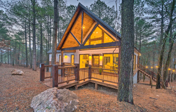 Image of a large cabin at dusk in Broken Bow, OK with an accessible front porch, decorated with outdoor lighting and surrounded by trees in the forest