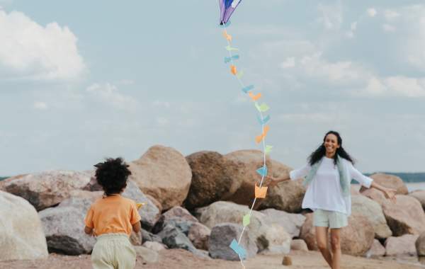 Image of a mother and child flying a kite on a beach family vacation with a large rock wall in the background