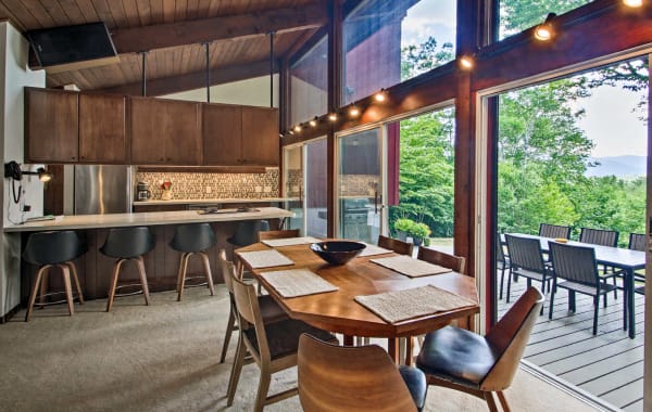 Image of a vacation rental interior with a dining room table and seating for 7 in the foreground, as well as a kitchen in the background with 4 chairs at the island.