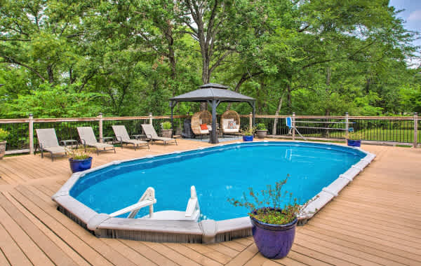 Wooden deck with a large pool and deck furniture, surrounded by trees