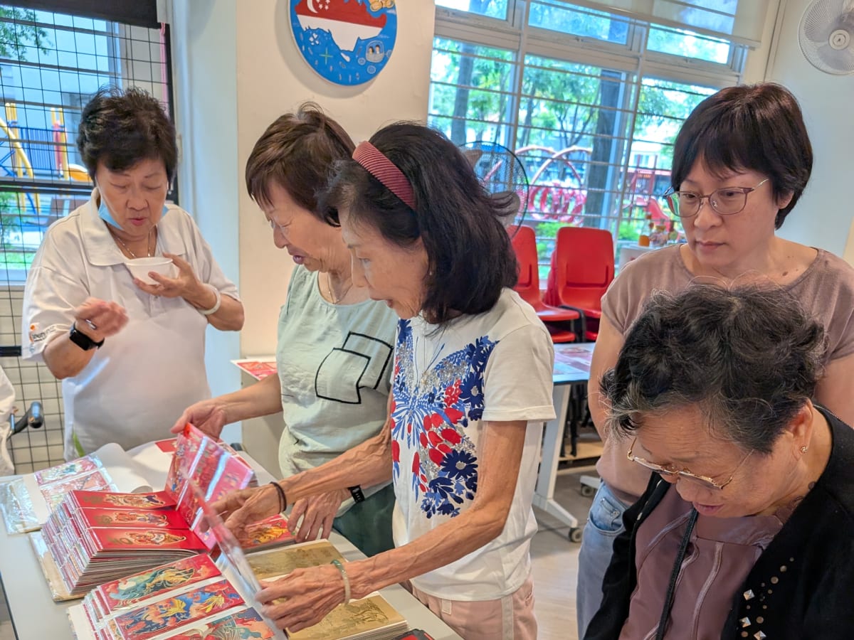 Seniors looking through albums of red packets at Our Treasure Box