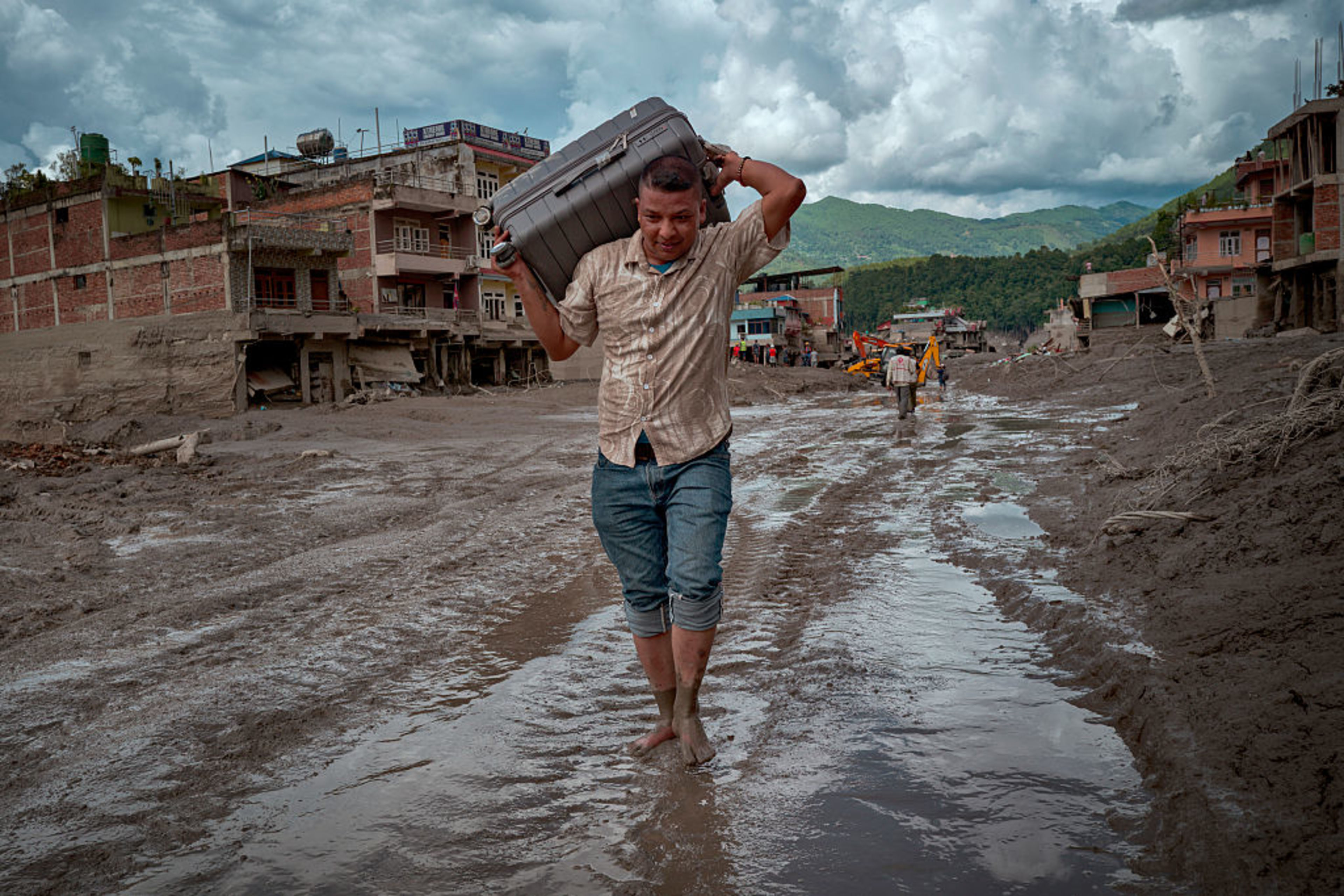 A resident carries belongings across a road heavily covered in mud following flash floods on Aug. 27, 2026, in Trishuli, Nepal. A sudden flood swept through the Bhote Koshi River basin in northern Rasuwa on Aug. 26, damaging settlements, roads, and energy infrastructure as rescue teams searched for residents and foreign travelers reported out of contact. Hundreds were reported missing as the death toll started to climb. | Credit: Ezra Acayan/Getty Images