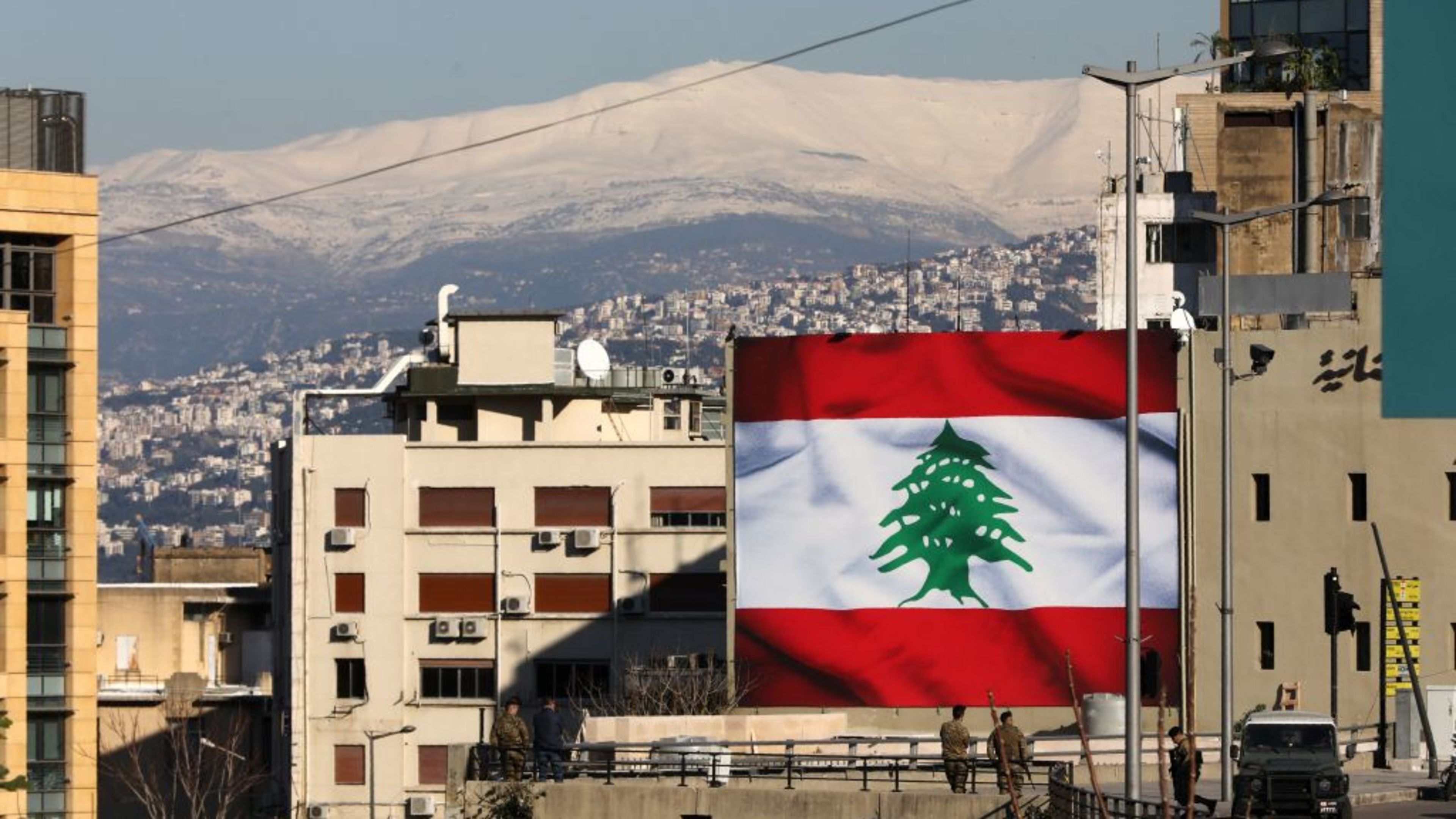 A picture taken on Jan. 25, 2020, shows Lebanese soldiers standing guard beneath a giant national flag in the capital, Beirut, with a backdrop of snow-covered mountains. | Credit: ANWAR AMRO/AFP via Getty Images