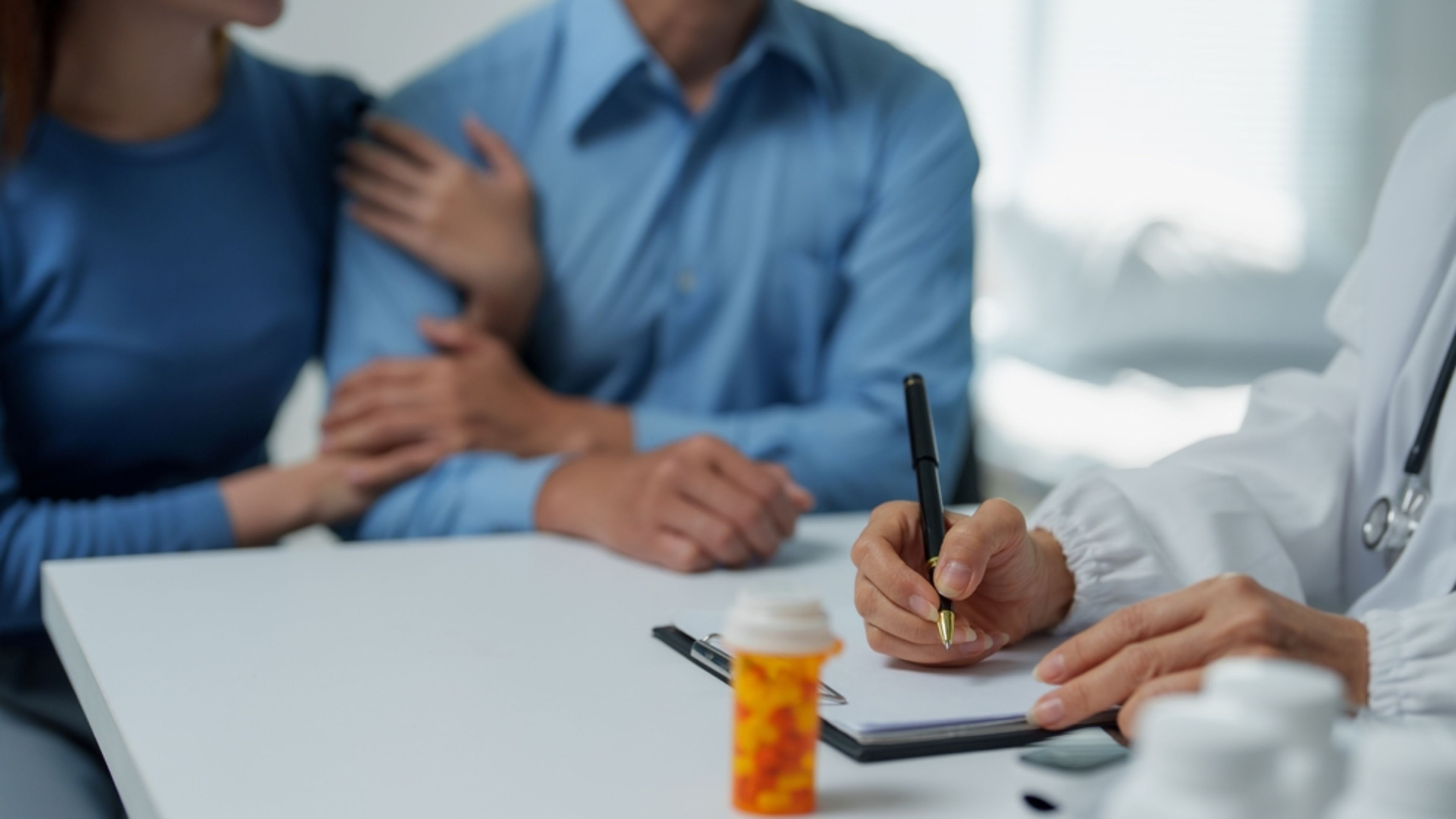 A doctor writes a prescription while a couple comforts each other. | Credit: PreciousJ/Shutterstock