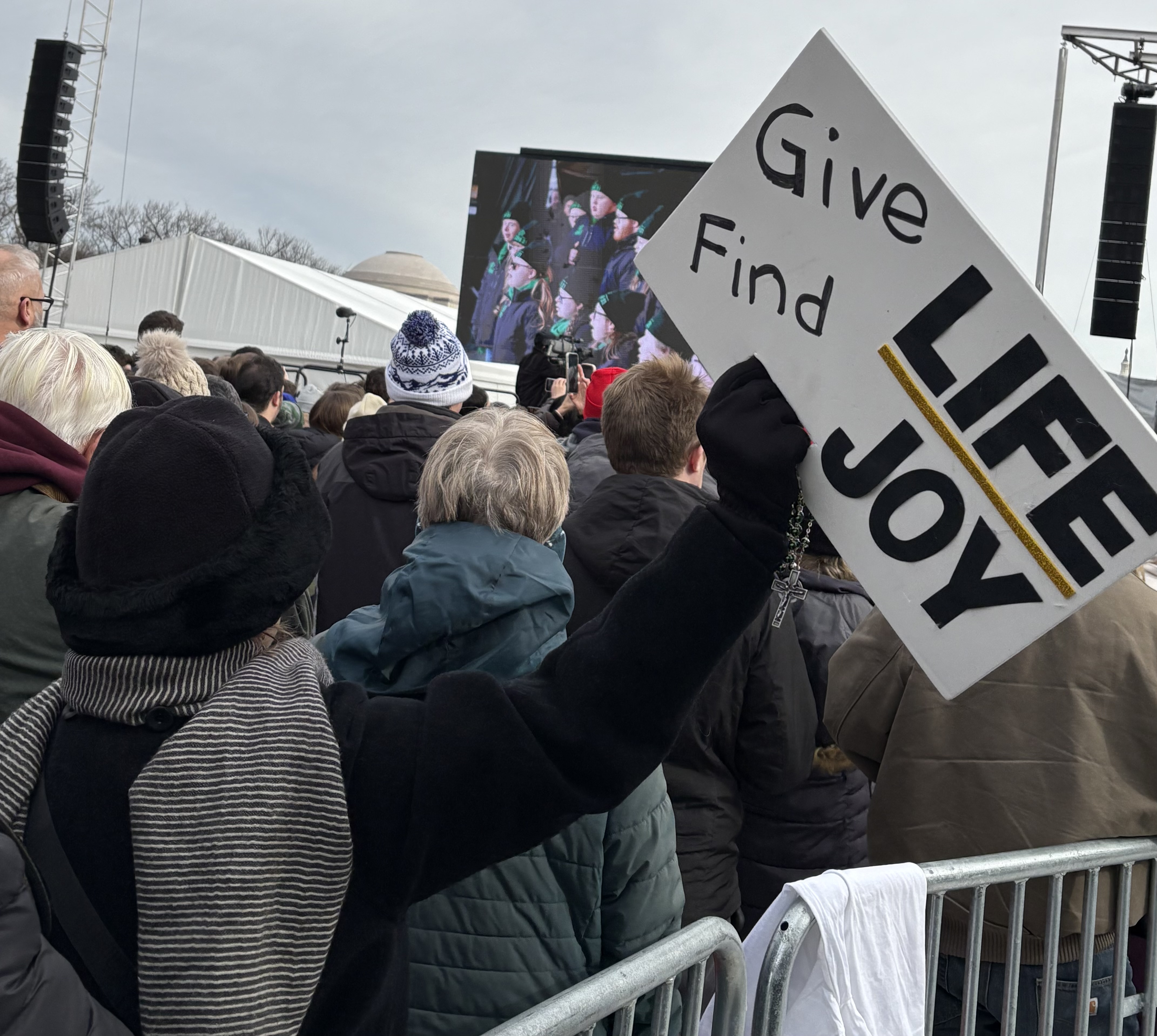 A woman waves her rosary and "Give Love Find Joy” sign during the national anthem at the March for Life Rally on Jan. 23, 2026. | Credit: Tessa Gervasini/EWTN News
