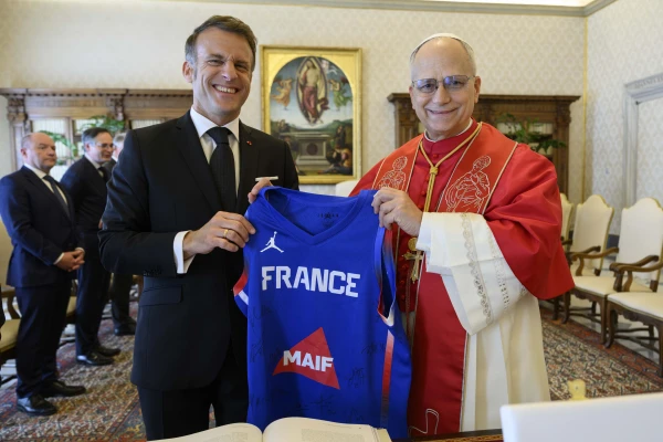 French President Emmanuel Macron presents Pope Leo XIV with a French national basketball team jersey in a meeting at the Vatican on April 10, 2026. | Credit: Vatican Media