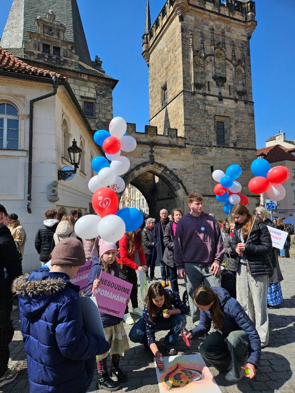 Children and families gather near the Lesser Town Bridge Tower in Prague with pro-life signs and balloons during the March for Life on April 11, 2026. Signs read “We do not judge, we help.” | Credit: Hnutí Pro život ČR