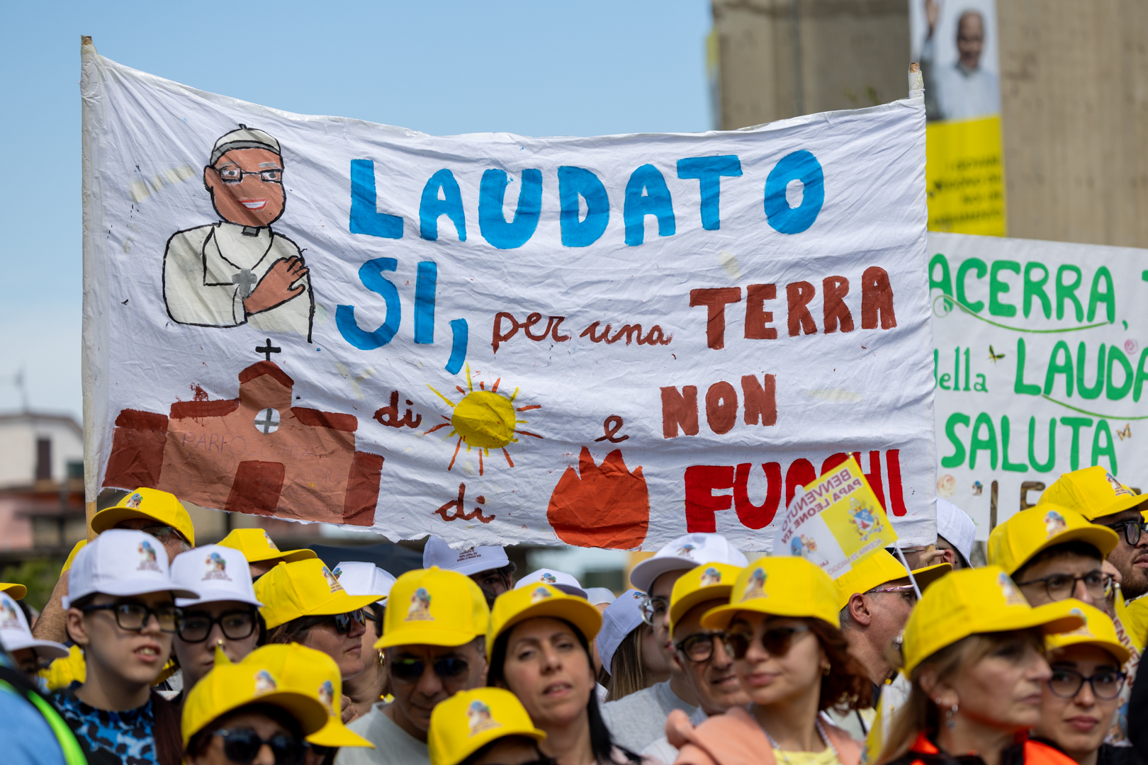 Crowds hold up signs as Pope Leo XIV makes an address in the Piazza Calipari in Acerra, Italy, May 23, 2026. The pope was visiting the “Land of Fires,” a region in southern Italy devastated by illegal waste dumping. | Credit: Daniel Ibáñez/EWTN News