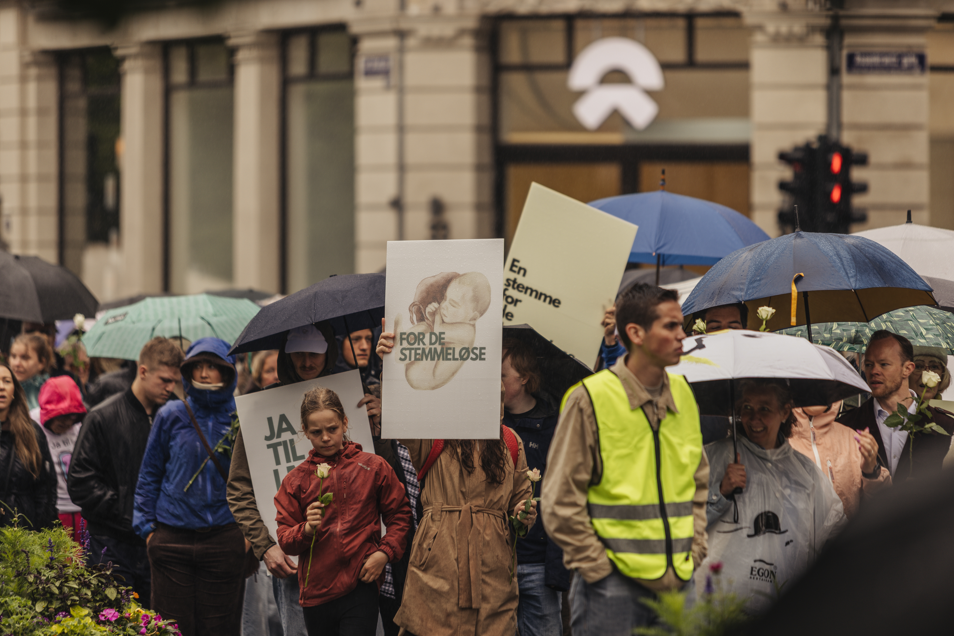 Participants walk under umbrellas in the rain, one holding a sign reading