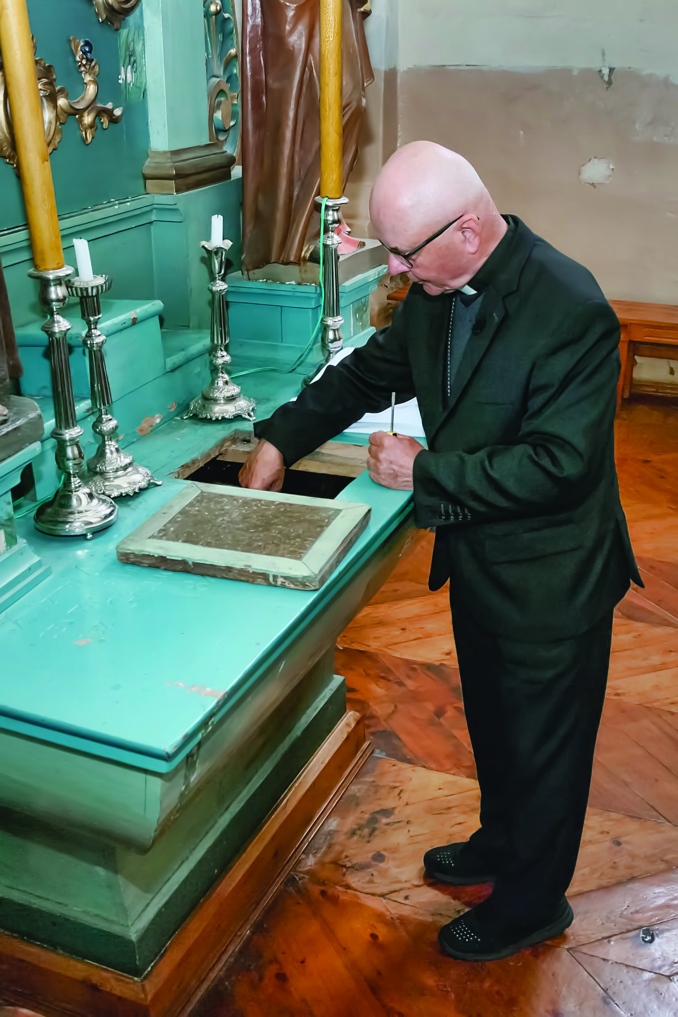 Cardinal Sigitas Tamkevičius reaches into the hiding place in the altar of the church in Simnas, Lithuania, where he once concealed copies of the underground Chronicle of the Catholic Church in Lithuania, in 2021. | Credit: Jūratė Tamošiūnytė-Karašauskienė