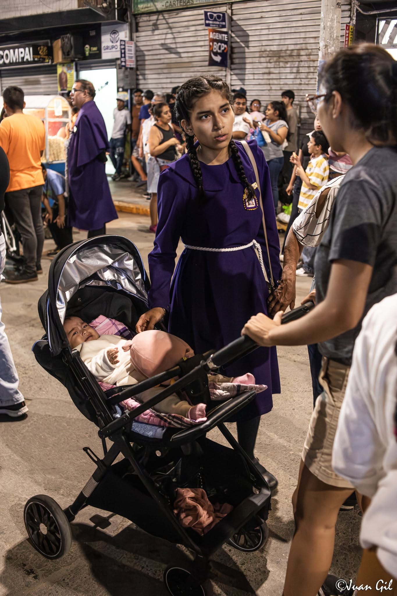 Transmisión de la tradición. Una joven sahumadora con el hábito morado cuidando a un bebé en su coche en medio de la calle. Foto: Juan Gil