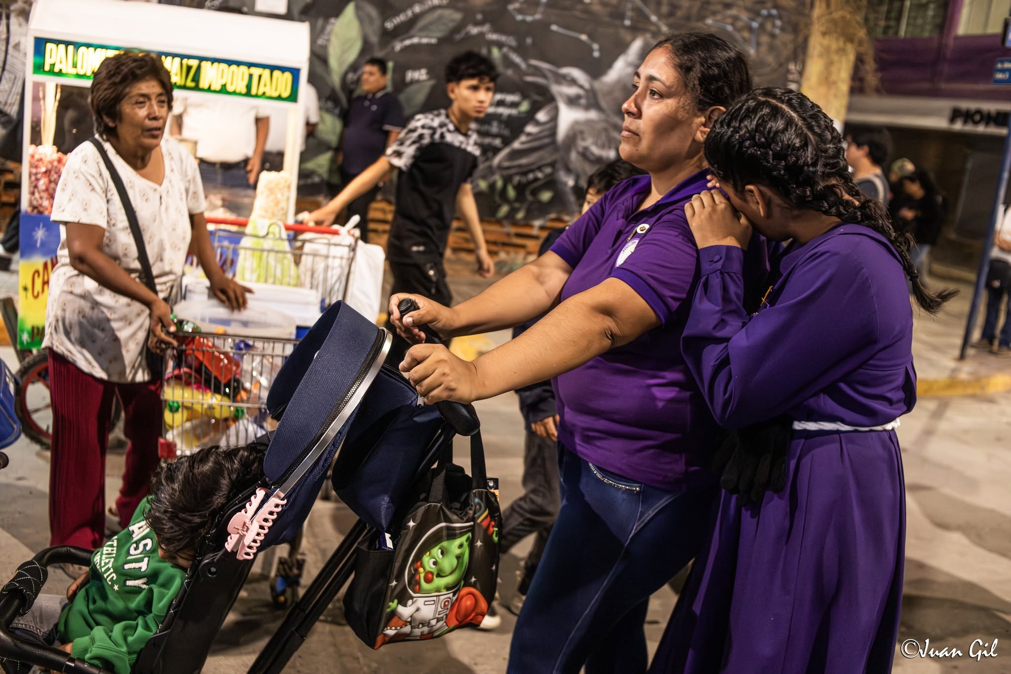 Emoción y consuelo familiar. Dos devotas unidas en oración junto a un coche de bebé; una de ellas llorando sobre el hombro de la otra. Una toma sumamente íntima. Foto: Juan Gil