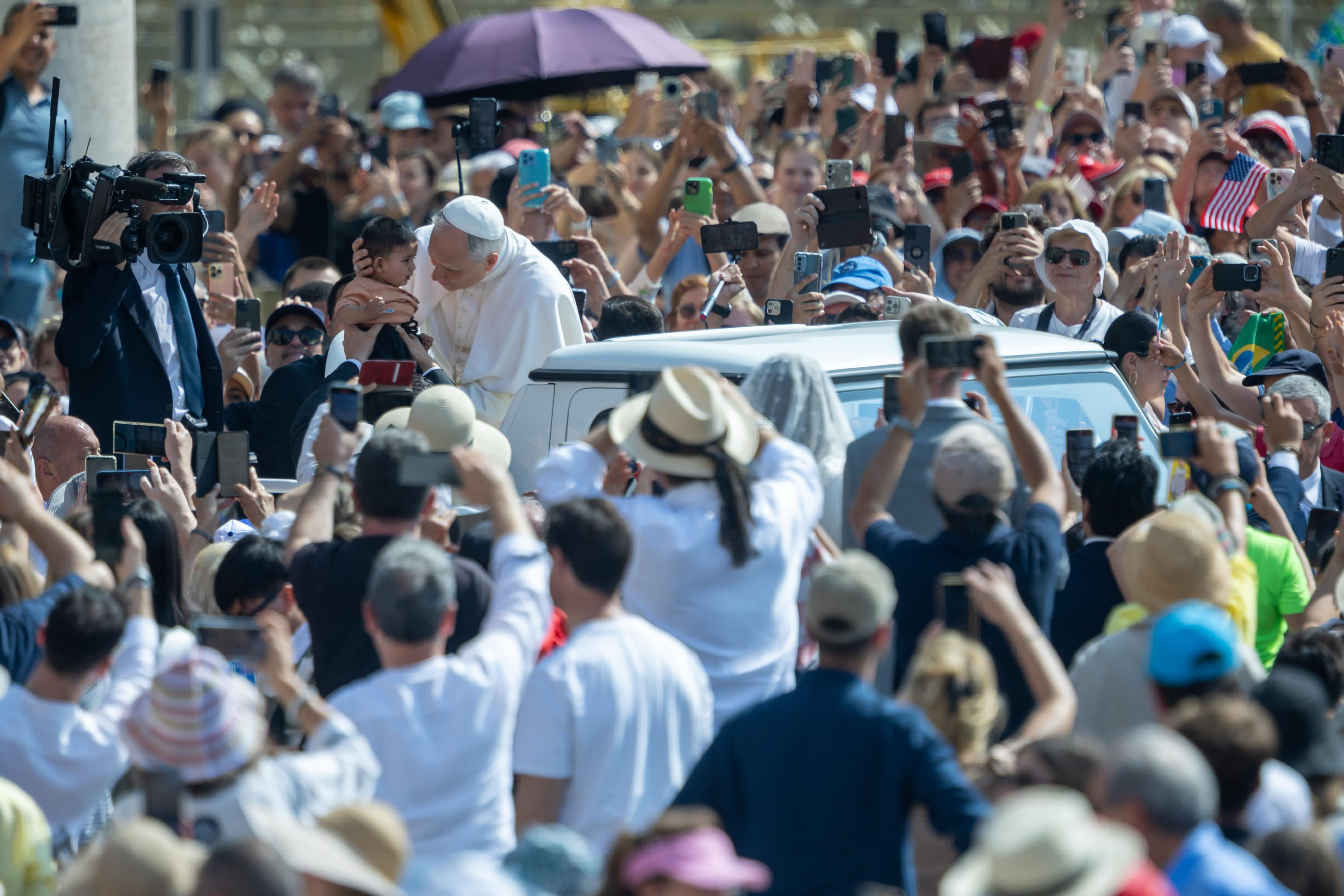 Paus Leo XIV omhelst een baby tijdens een rit over het Sint-Pietersplein in de pausmobiel vóór de algemene audiëntie op 11 juni 2025. Credit: Daniel Ibanez/CNA