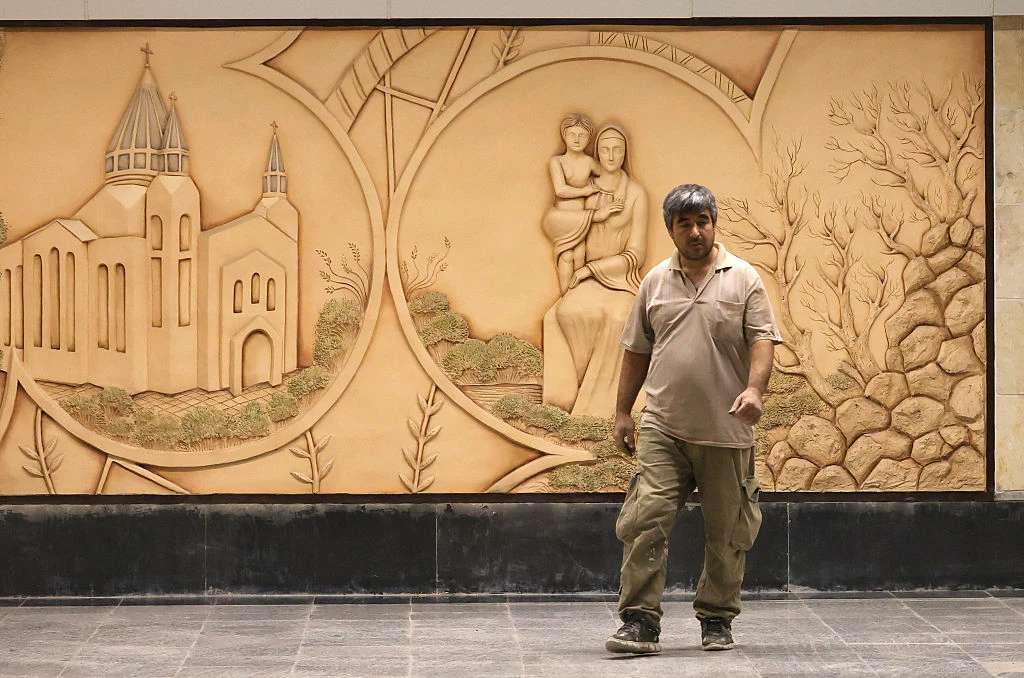 Een Iraanse arbeider loopt voor een reliëfsculptuur van de Heilige Maagd Maria bij het pas geopende Maryam Moghaddas (Heilige Maagd Maria) metrostation nabij de Sarkis Kathedraal van de Armeniërs in Teheran op 18 oktober 2025. Credit: ATTA KENARE/AFP via Getty Images