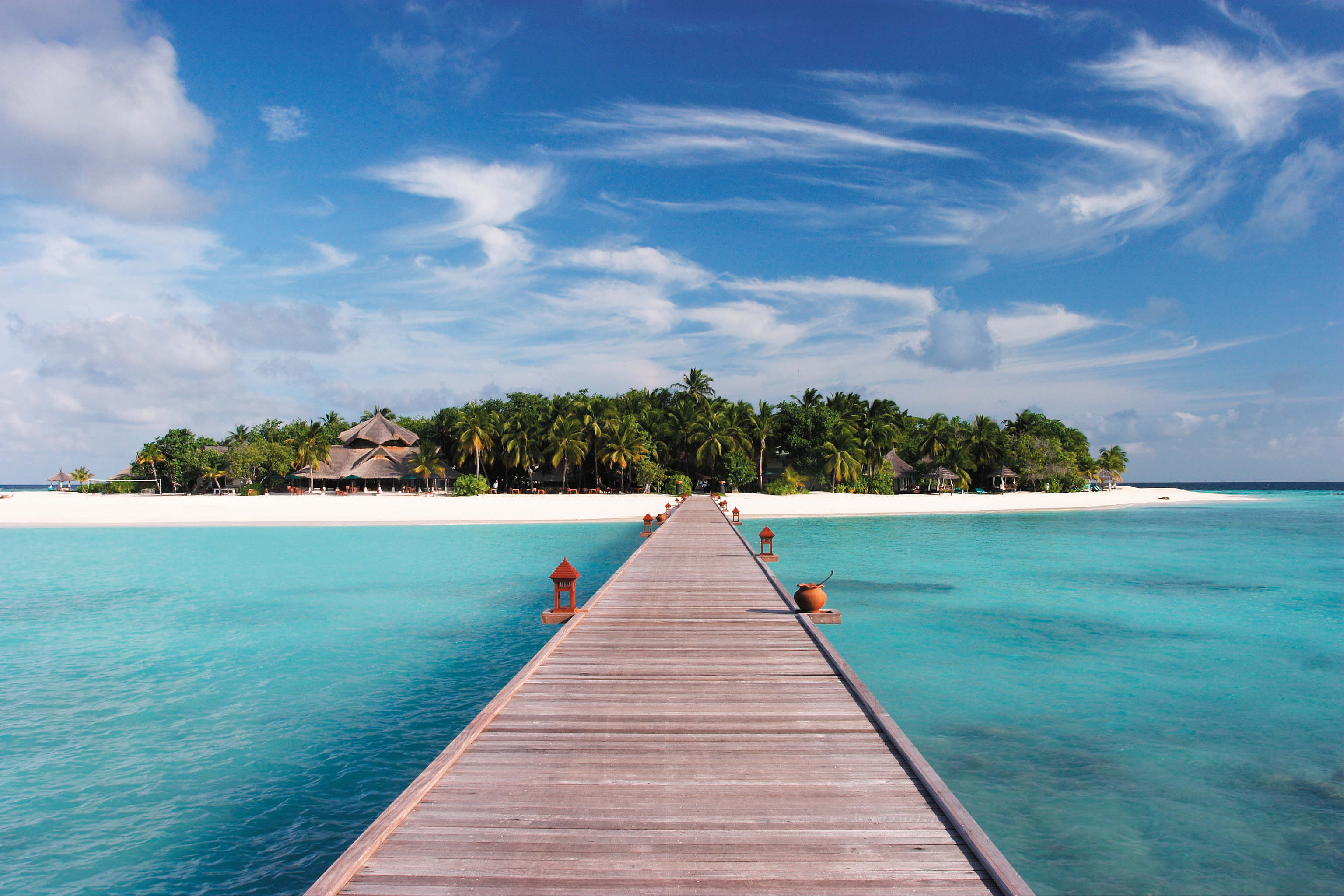 Wooden walkway leading to the entrance of Banyan Tree Resort in the Maldives, surrounded by turquoise waters and lush palm trees.