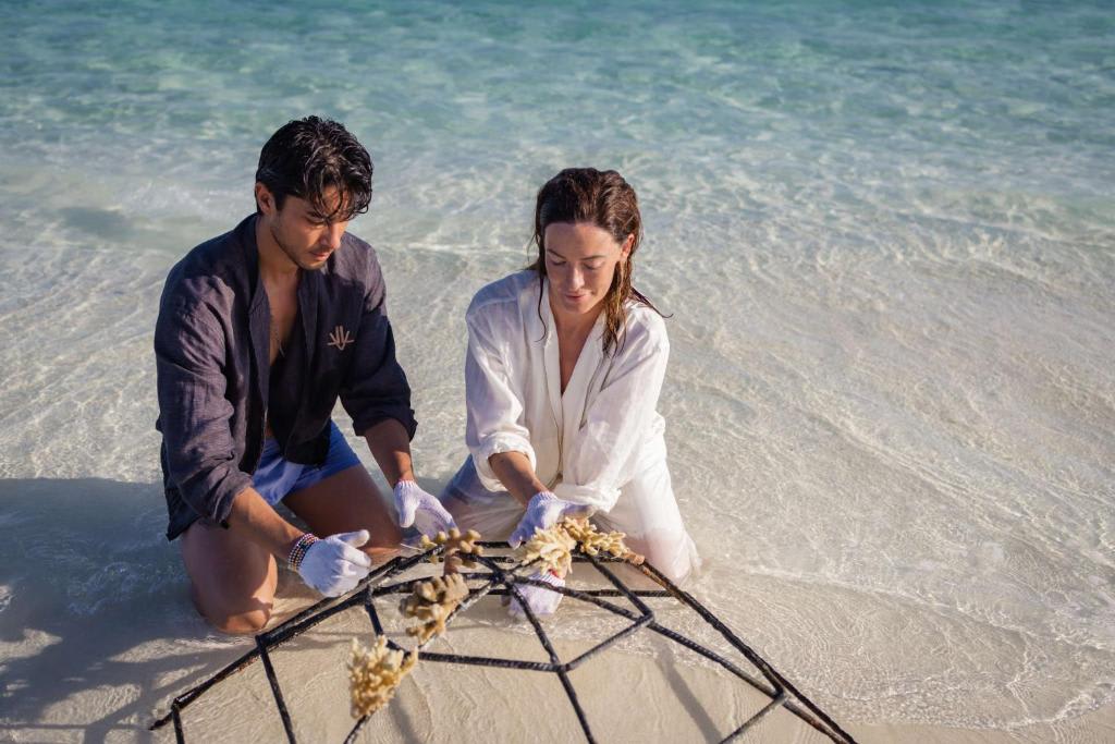 Couple planting coral in shallow waters on a beach in the Maldives as part of a conservation effort.