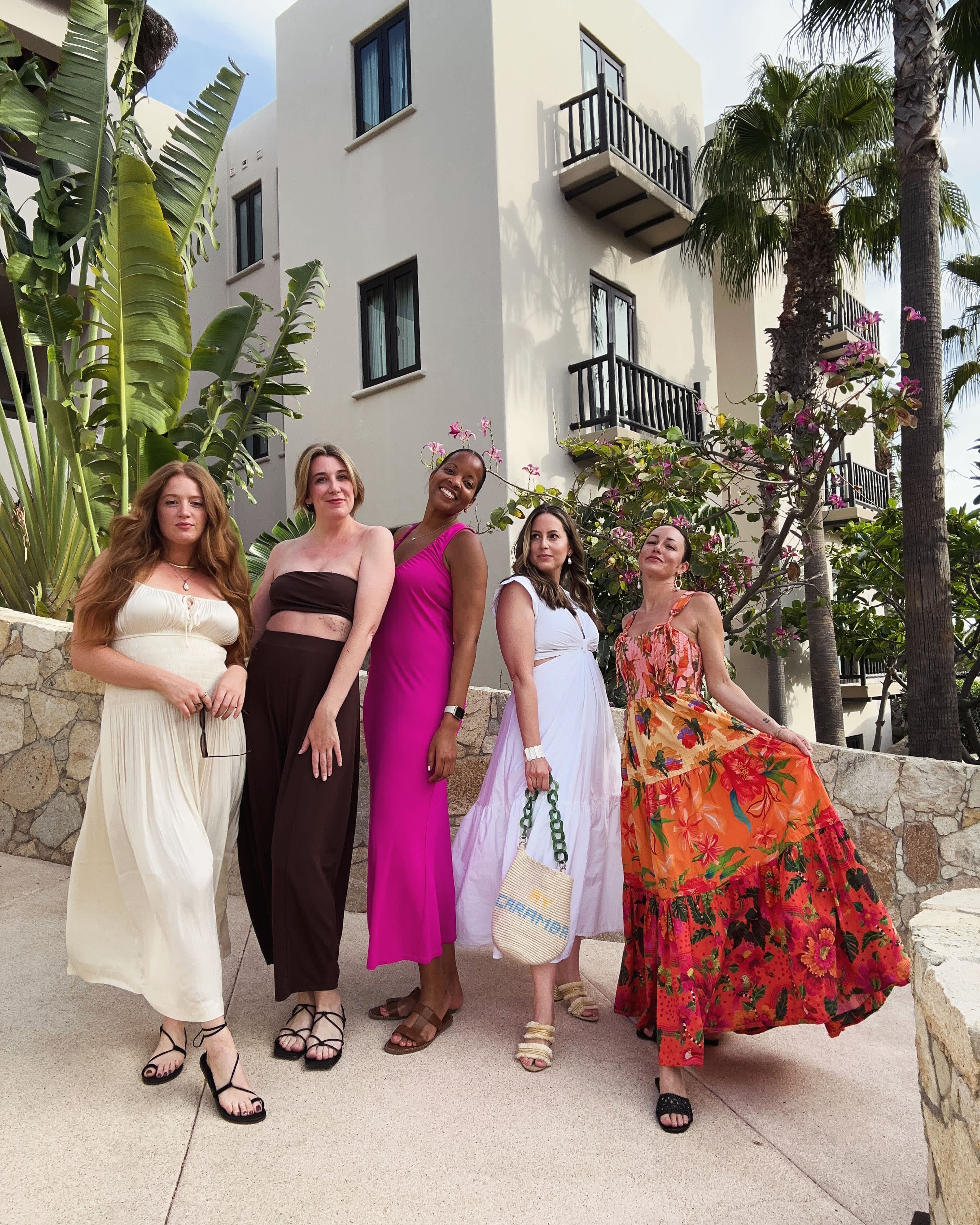 Group of women posing in colorful dresses in front of a resort building in Los Cabos, staying with Exclusive Resorts.