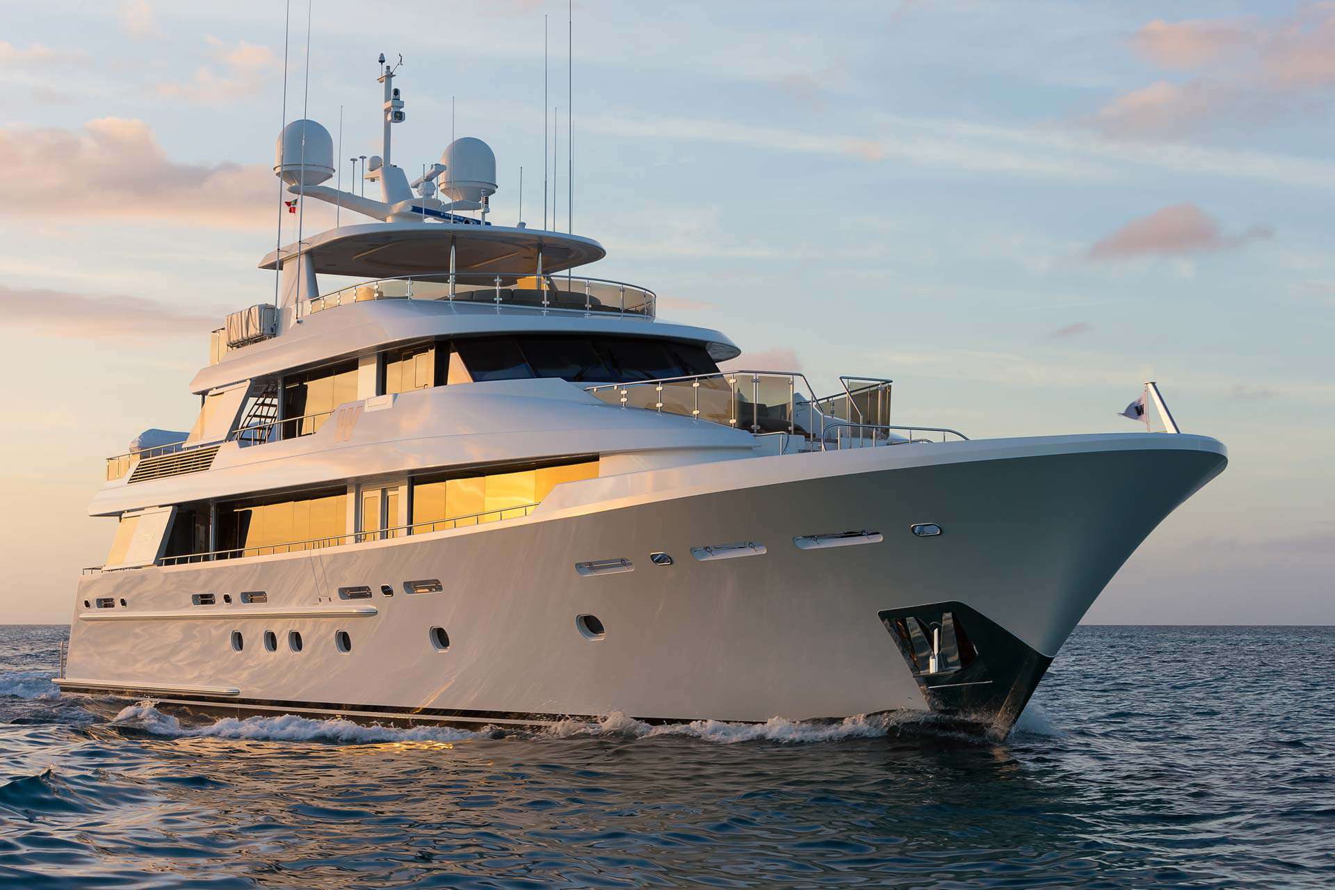 Luxury yacht cruising on the ocean at sunset with soft light reflecting off the water and the yacht's sleek exterior.