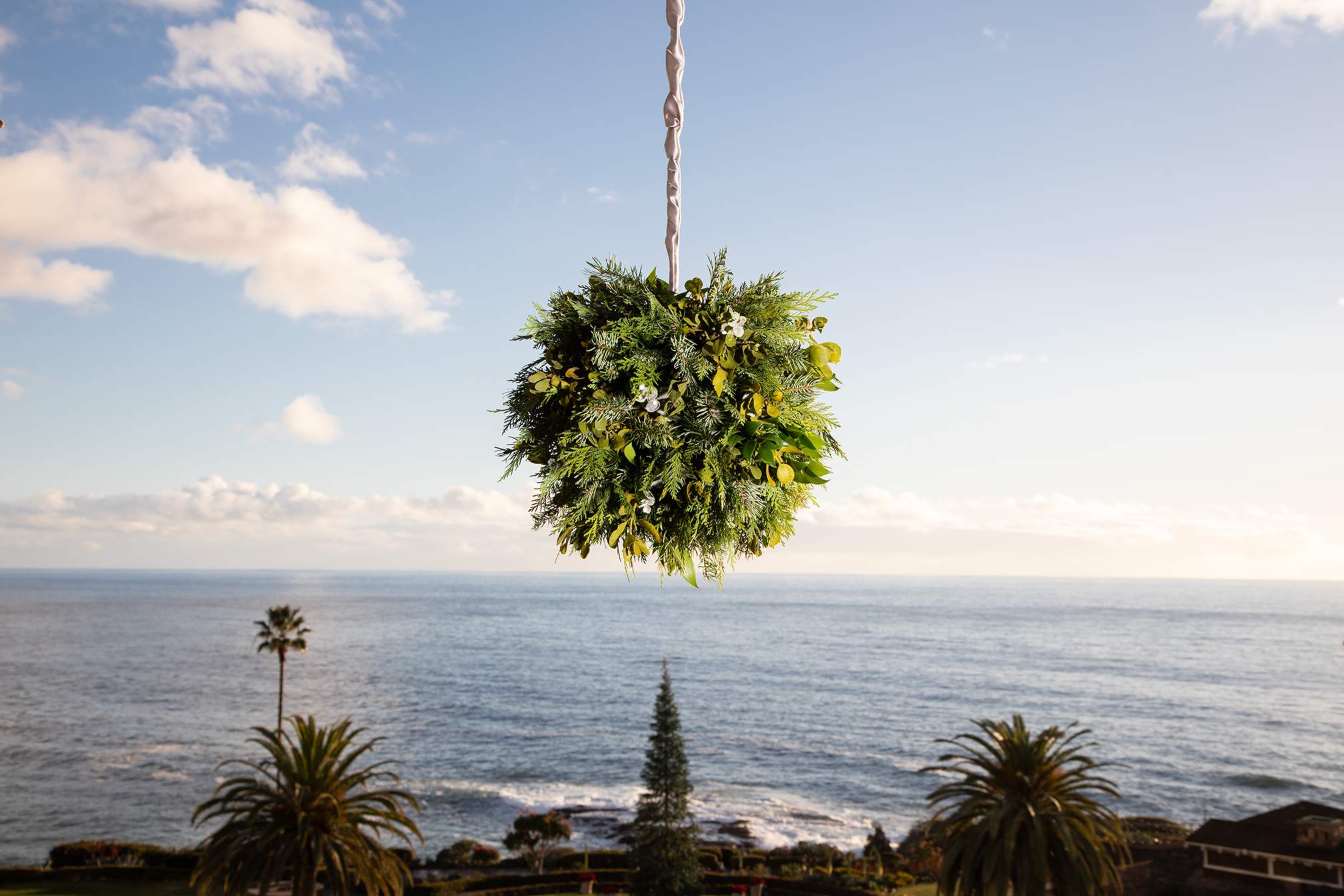 Mistletoe hanging with an ocean view backdrop at Montage Laguna Beach, framed by palm trees and a Christmas tree in the distance.