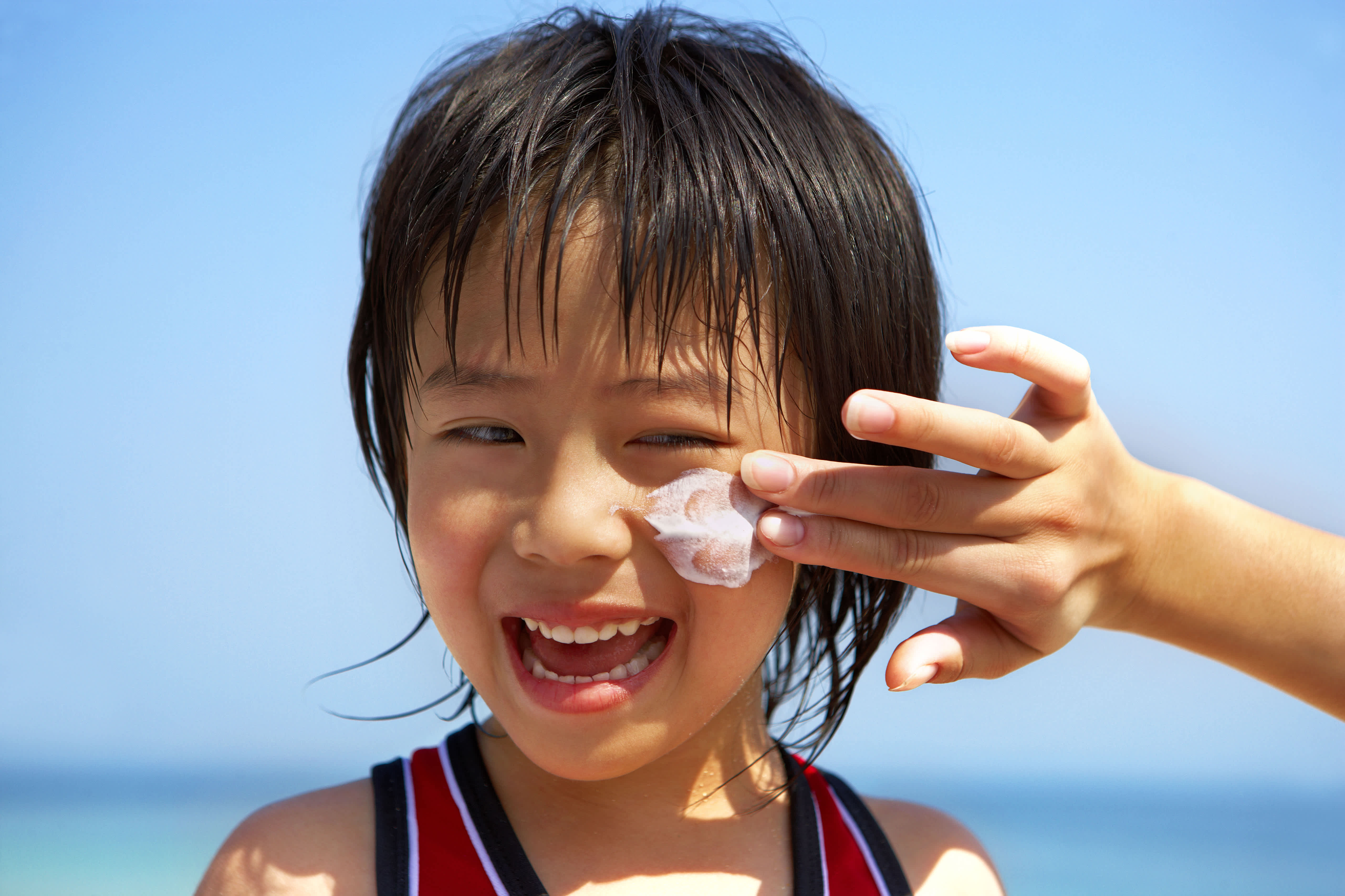 Child laughing while sunscreen is applied to their face at the beach.