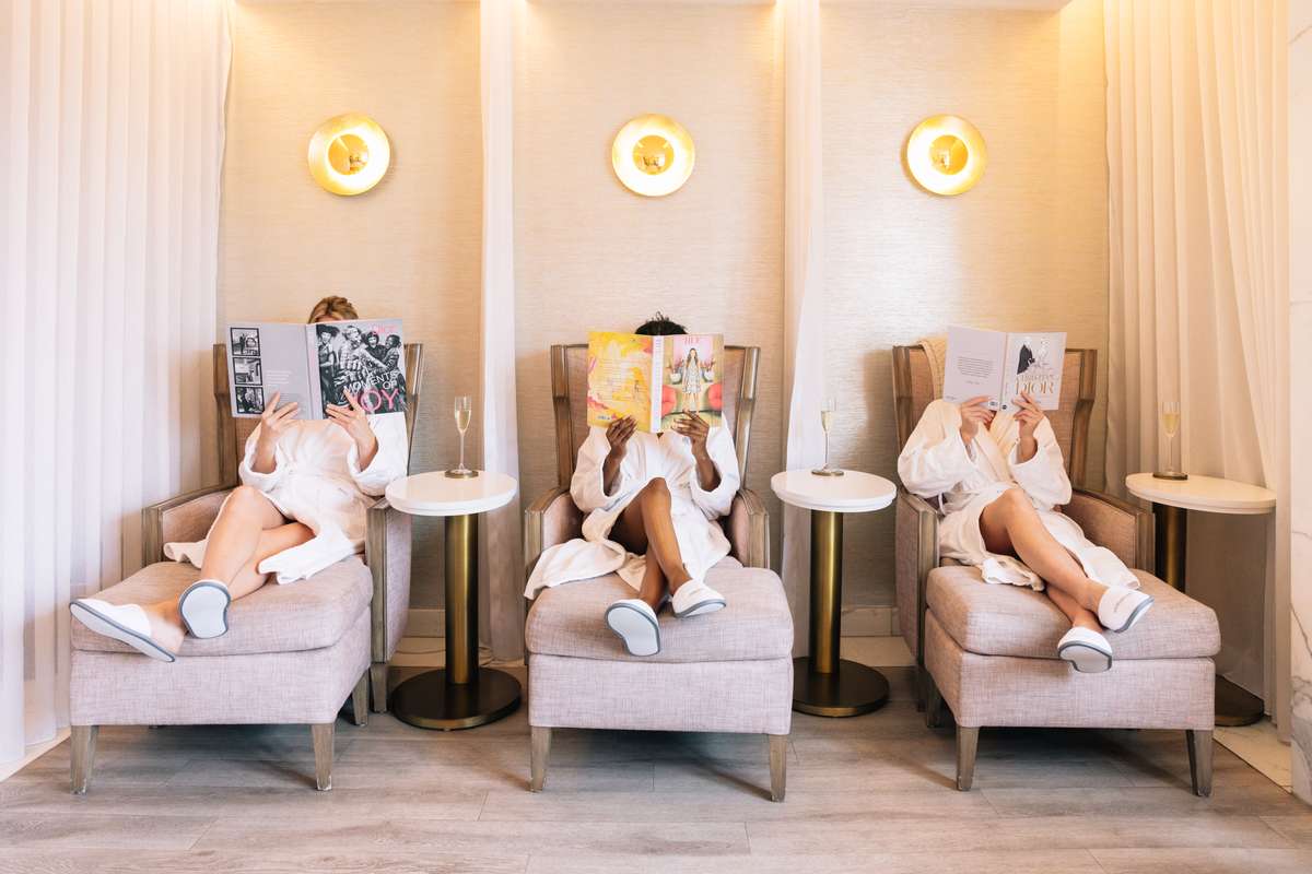 Three women relaxing in lounge chairs with magazines at The Peninsula Beverly Hills spa.