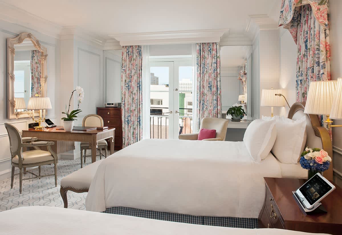 Elegant twin bedroom in The Peninsula Beverly Hills hotel with a desk, mirror, and floral decor.