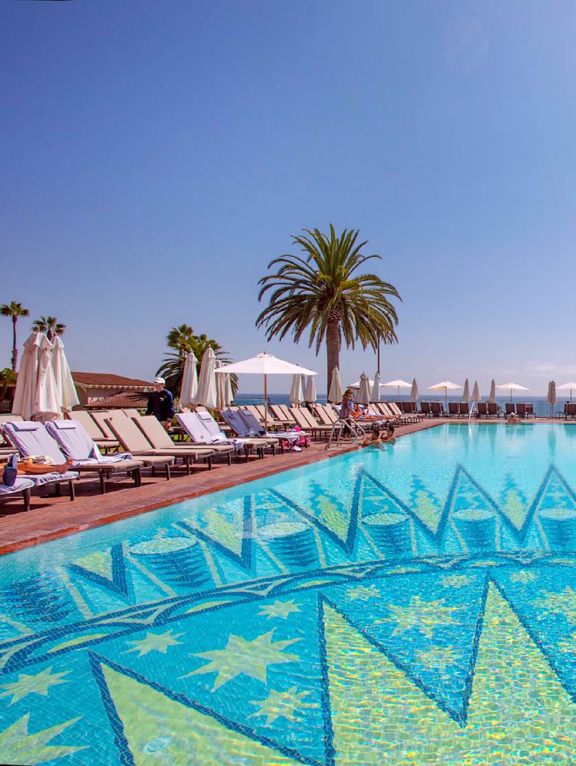 Luxurious poolside at Montage Laguna Beach with palm trees and ocean view in the background.