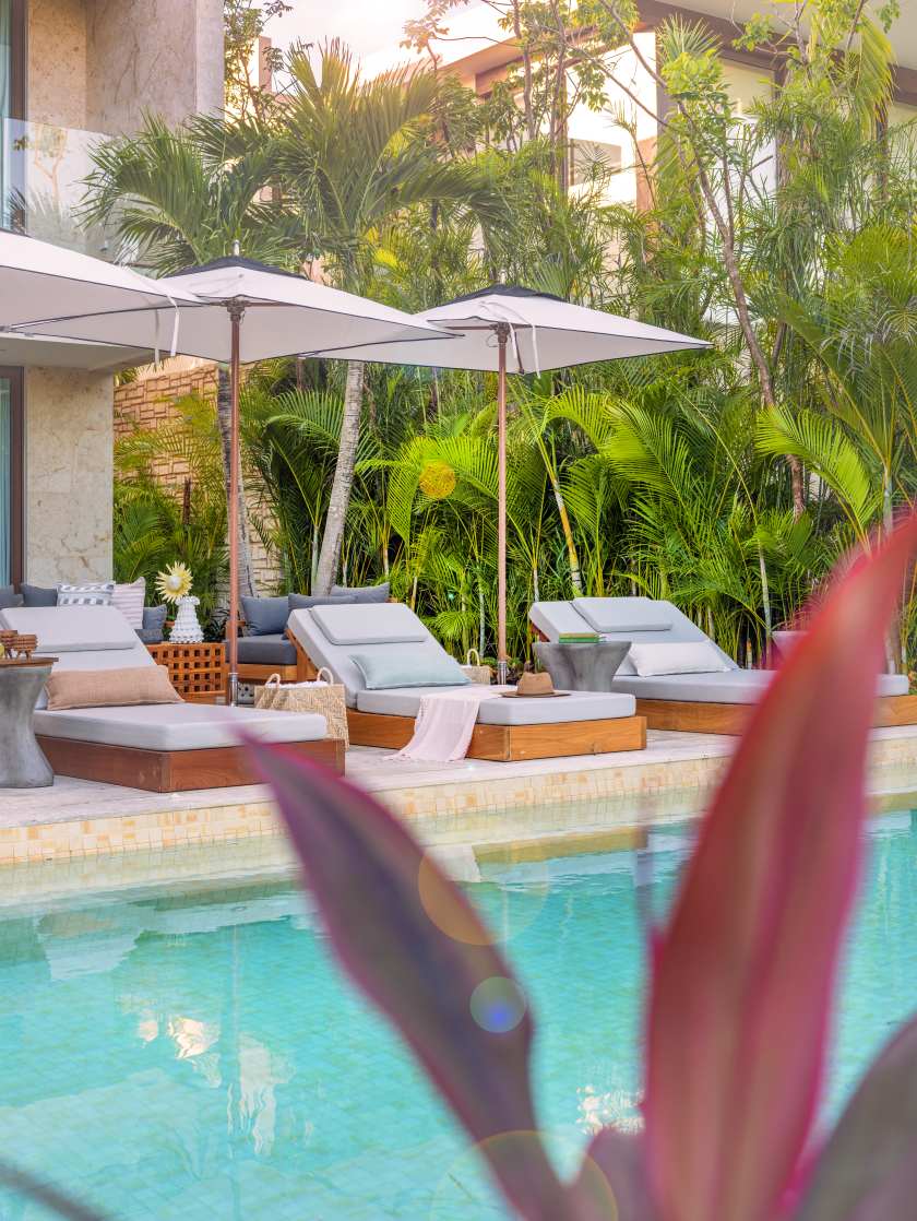 Lounge chairs with umbrellas beside a serene pool surrounded by lush greenery at Rosewood Mayakoba.