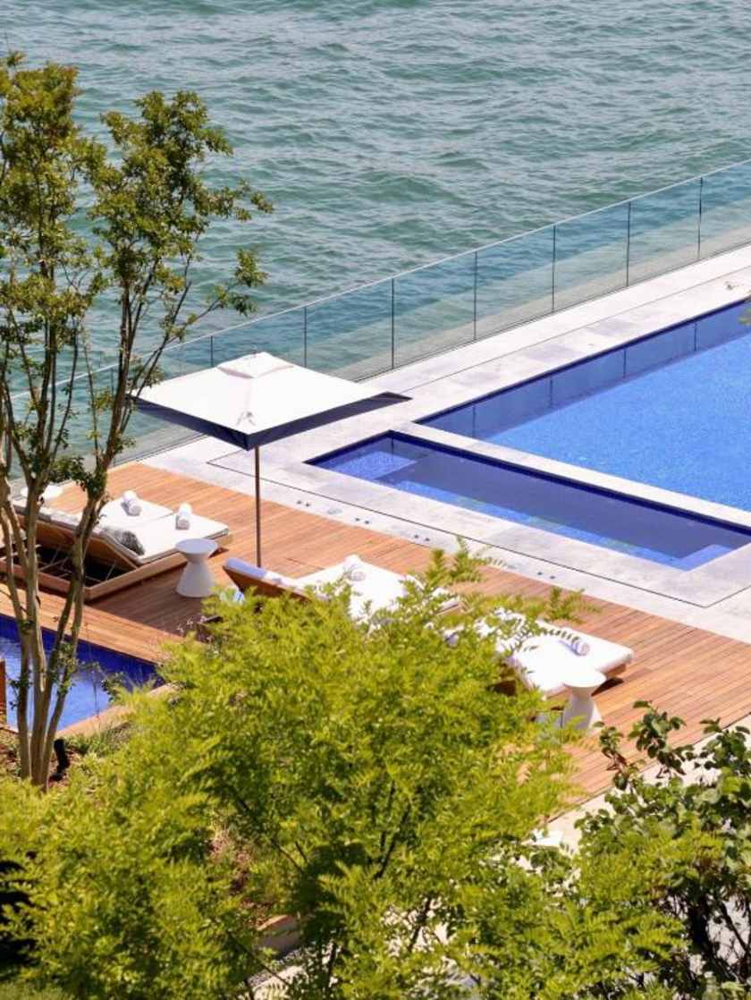 Infinity pool and lounge chairs overlooking the water, surrounded by greenery at Istanbul Peninsula Hotel.