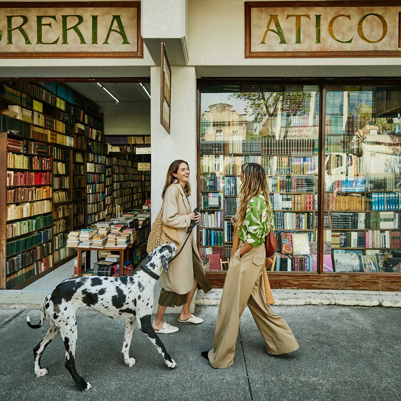 Two women walking a dog in front of a bookstore in Mexico City.