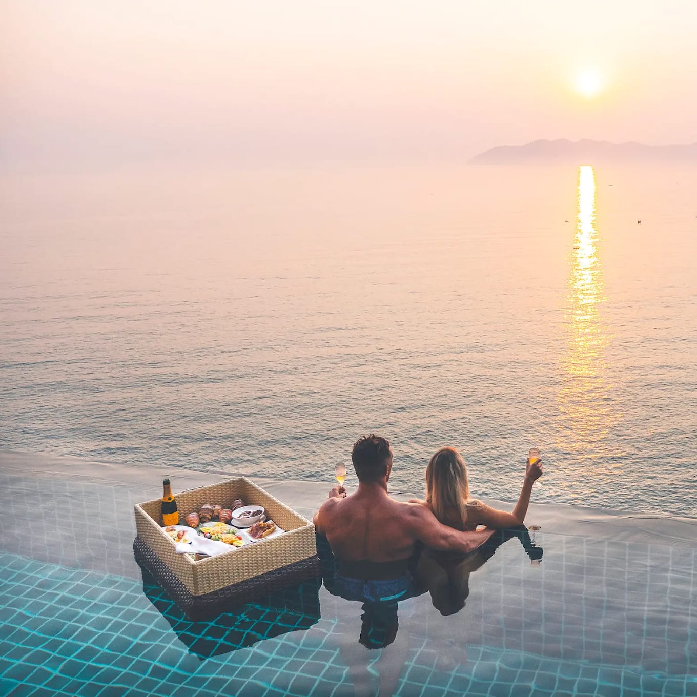 Couple enjoying a sunset view from an infinity pool with a floating breakfast in Lang Co, Vietnam.