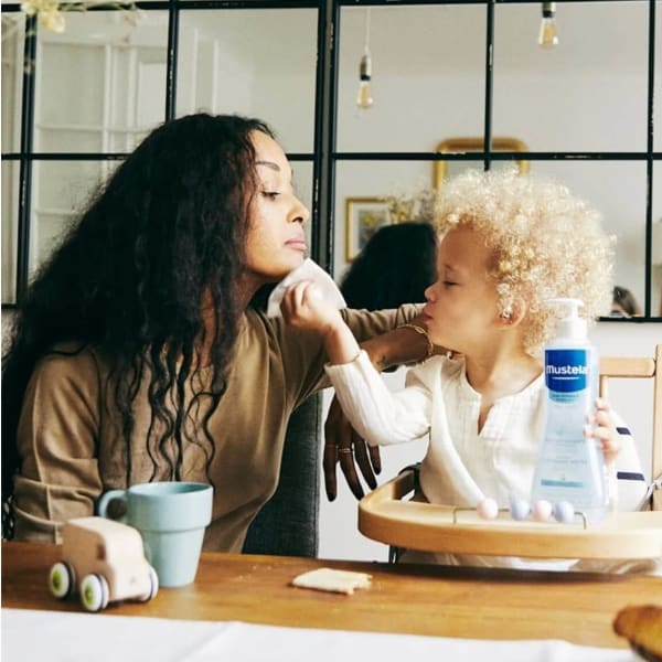 Een klein meisje veegt het gezicht van haar moeder af met een Mustela-product