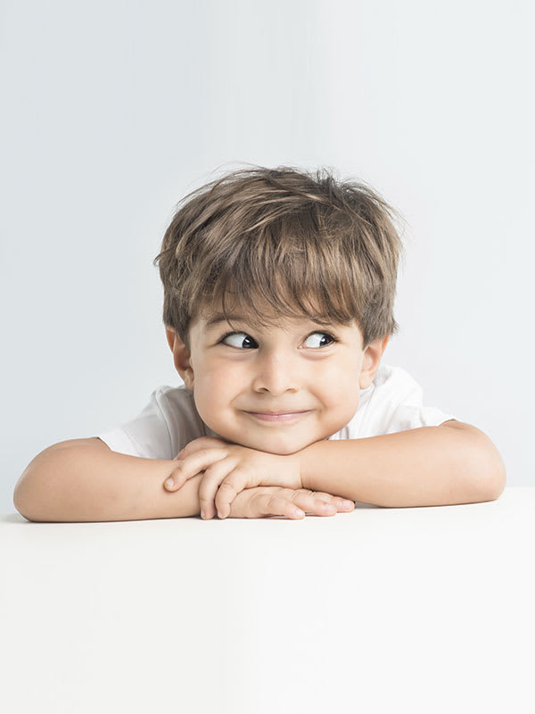 Child lying on his stomach with his head resting on his arms crossed and looking to the right