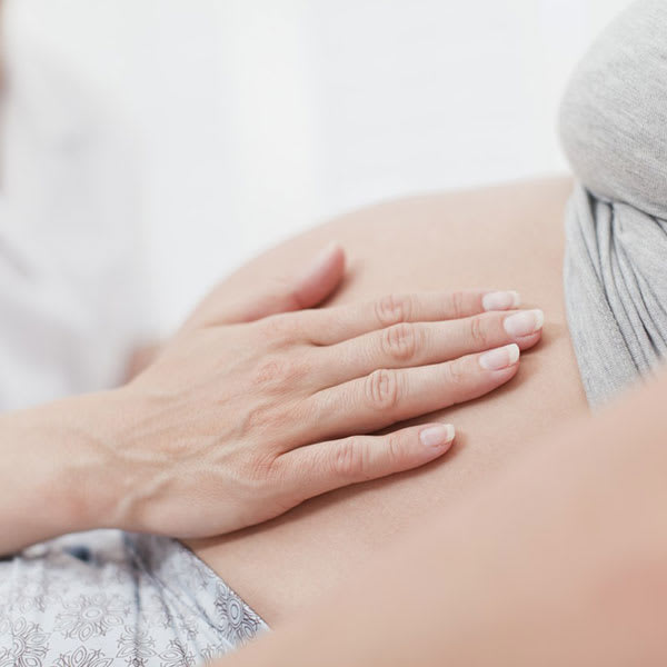 De hand van een vroedvrouw op de buik van een zwangere vrouw