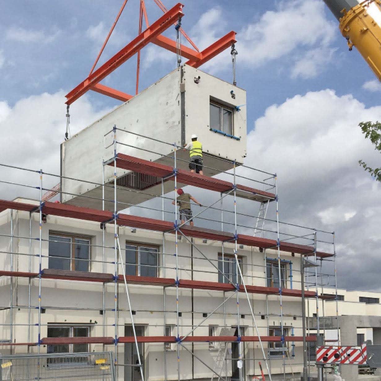 Prefabricated building module lifted by crane for installation on a multi-story housing project