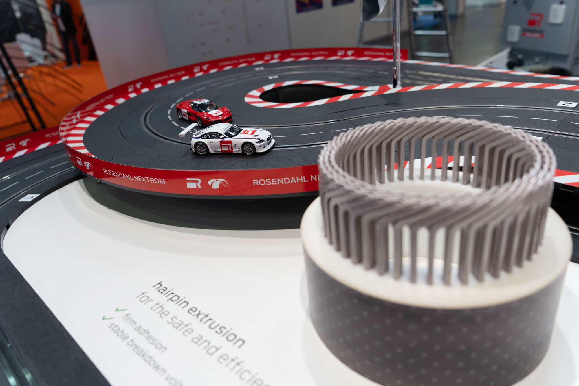 Exhibición de Rosendahl Nextrom con una pista de Scalextric y dos coches de slot miniatura, junto a una muestra de extrusión de horquilla y texto que resalta 'adhesión firme' y 'voltaje de ruptura estable'.