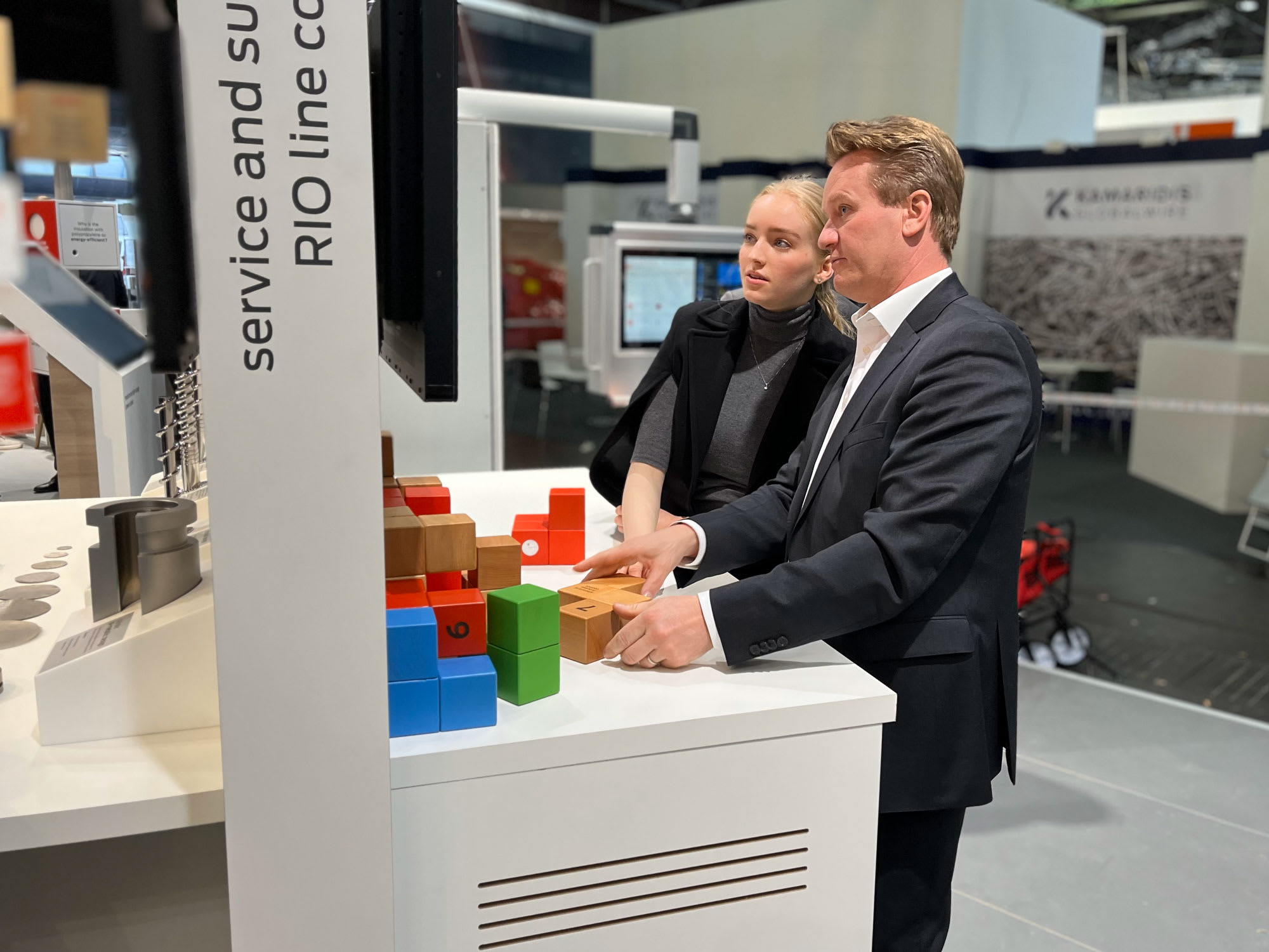 Man and woman interacting with a display of colorful, numbered blocks at a Kawaris industrial technology exhibition.