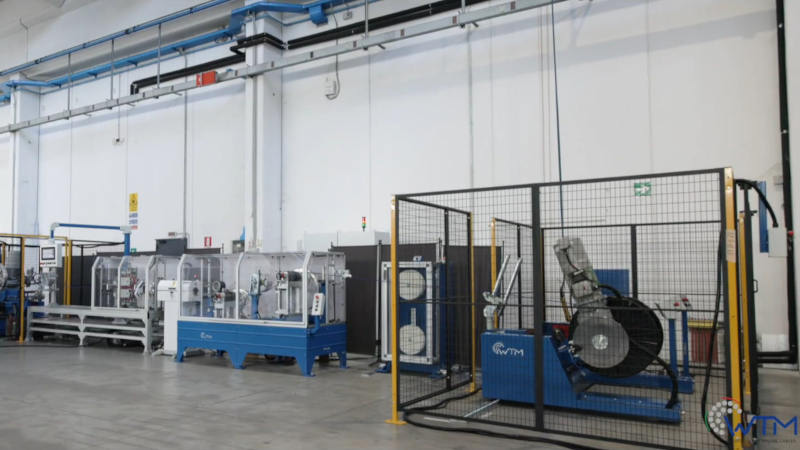 Linea di produzione WTM con macchinari industriali per la lavorazione di cavi, inclusi avvolgitori e sistemi di sicurezza, all'interno di un moderno stabilimento.