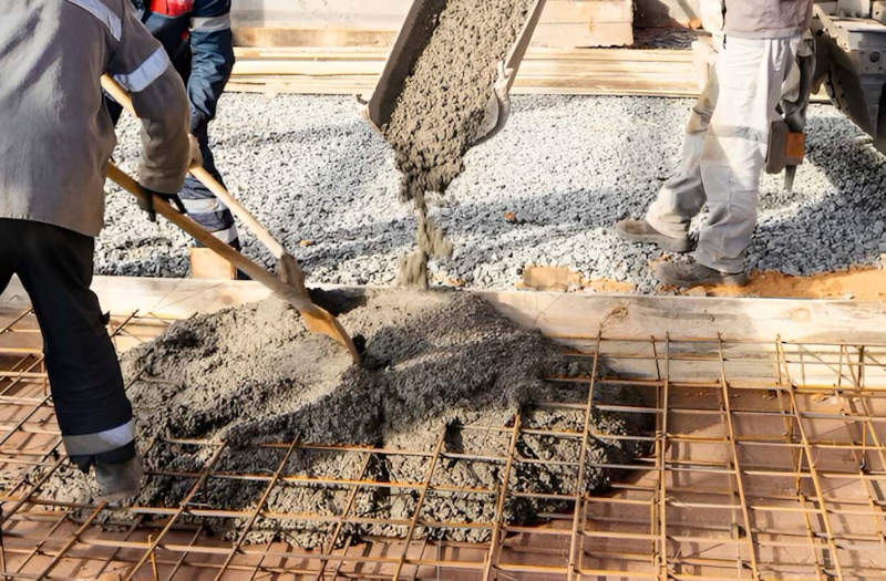 Construction workers pouring & spreading fresh concrete over a rebar grid for a building foundation.