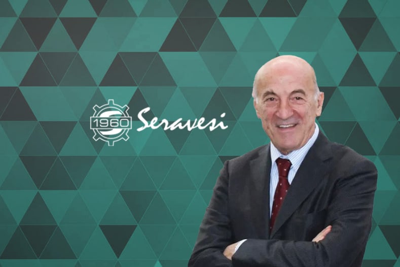 Smiling businessman in a dark suit and red tie, standing against a green geometric background featuring the Seravesi 1960 logo.