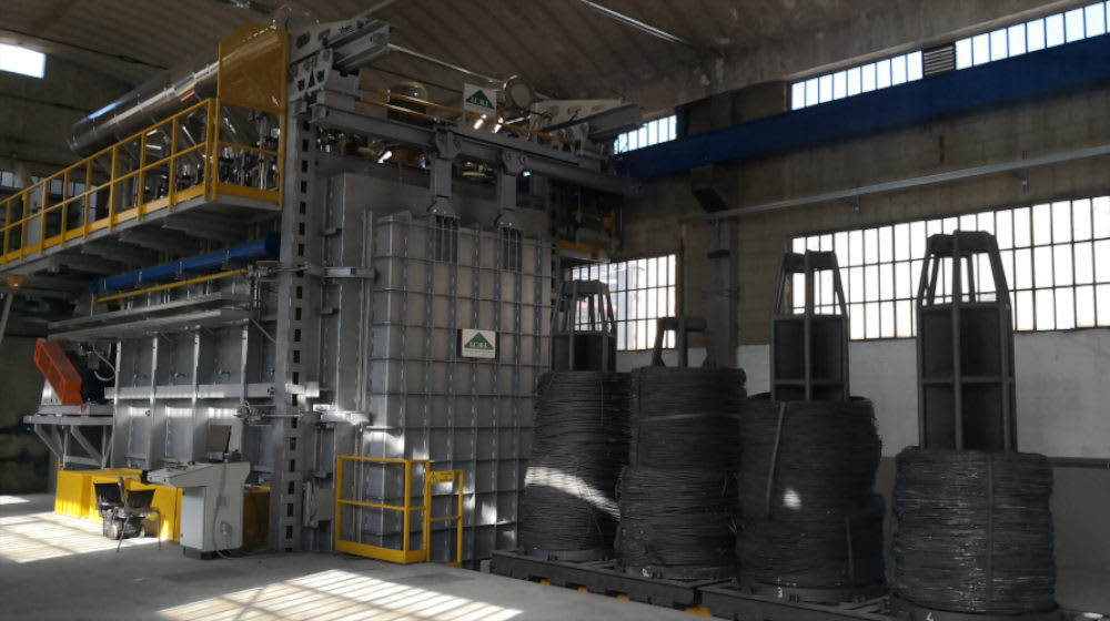 Advanced industrial annealing furnace for metal wire coils, with product stacked on pallets in a brightly lit manufacturing plant.